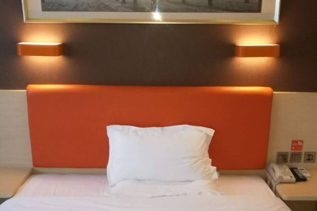 A hotel room with a bed, white pillow, orange headboard, and wall-mounted lights.