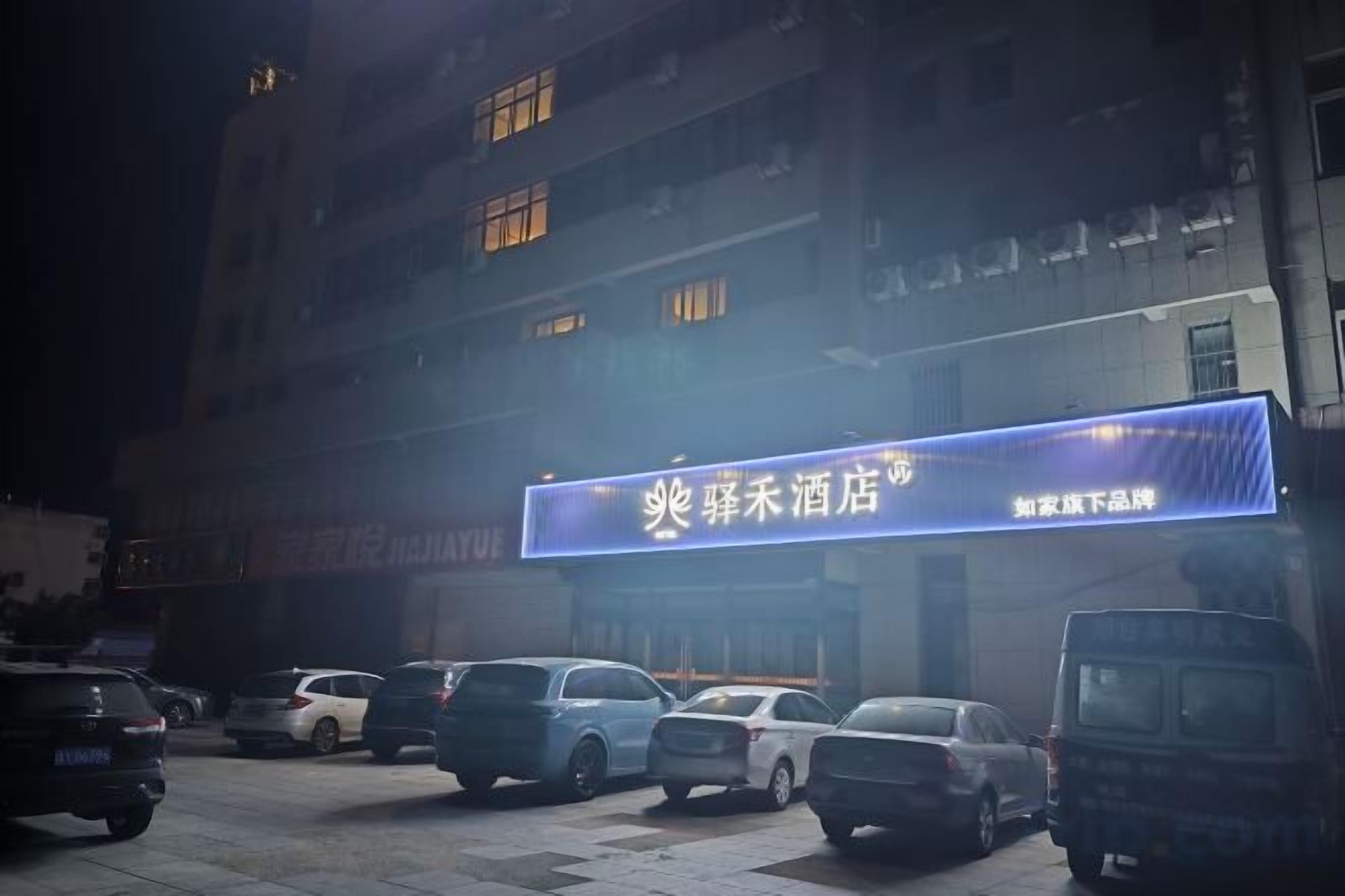 Un edificio con un cartel iluminado, autos estacionados y una camioneta en la entrada.
