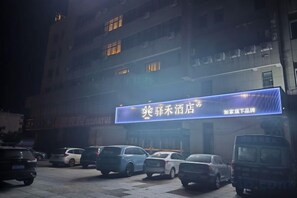 A building with a lit signboard, parked cars, and a van in front. - Home Inn Yihé Hotel (Yantai Zhaoyuan Puzhao Road Nandu Lijing Branch) (Zhaoyuan)