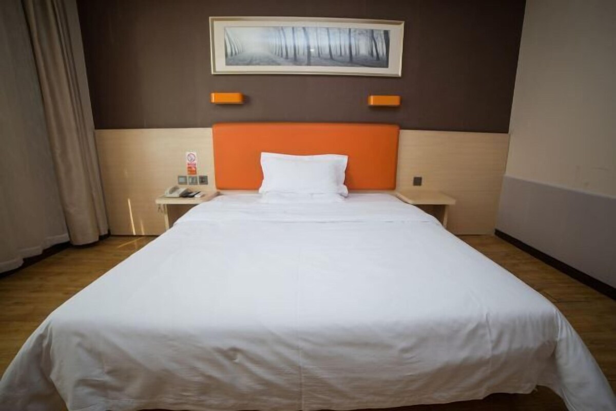 A hotel room with a large bed, a nightstand with a phone, and a painting on the wall.
