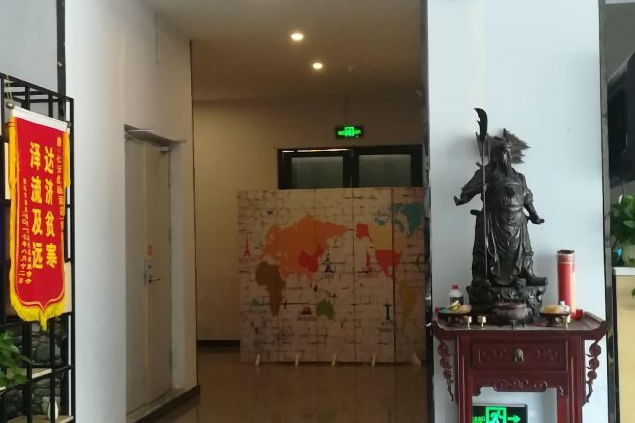 Un pasillo con una estatua sobre un pedestal, un mapa en la pared y un cartel rojo.