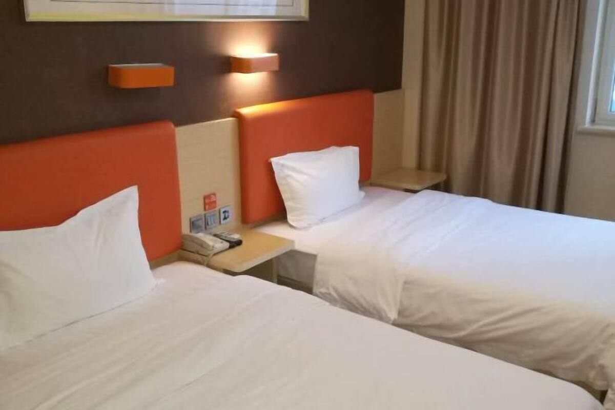 A hotel room with two beds, a nightstand with a phone, and a wall-mounted light.