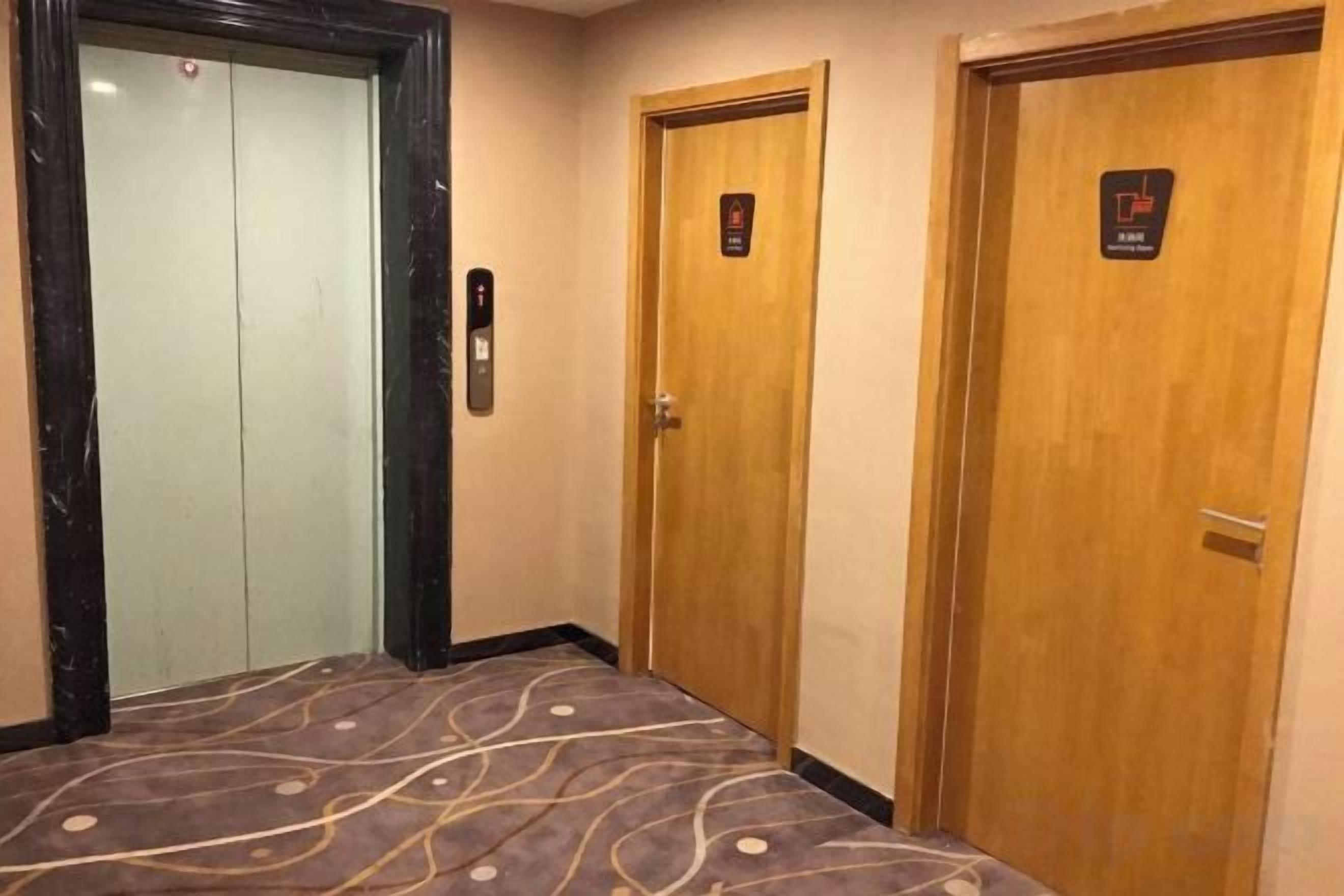A hotel room with a bed, a wooden door, and an elevator.