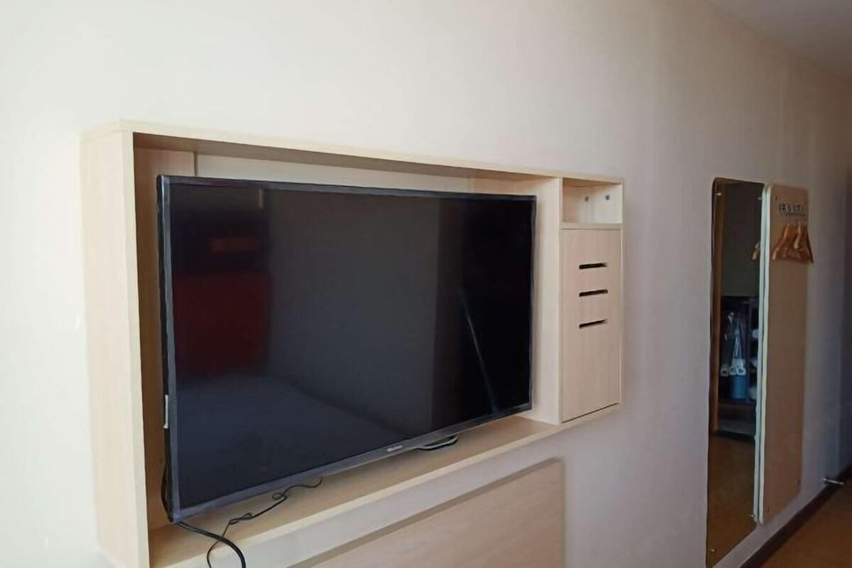 A room with a built-in TV, a wardrobe with hanging space, and a mirror.