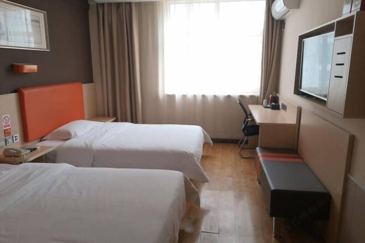A hotel room with two beds, a desk, a chair, a TV, and a window with curtains.