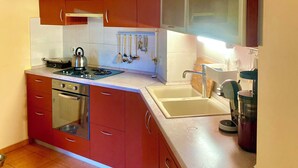 A compact kitchen with red cabinets, a stainless steel stove, a sink, and a window above the countertop. - Apartments Teo and Marin (Zagreb)