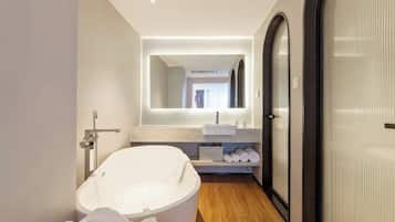 A modern bathroom with a freestanding bathtub, a large mirror, and a wooden floor.
