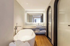 A modern bathroom with a freestanding bathtub, a large mirror, and a wooden floor. - Xiamen Aston Hotel (Zhongshan Road · Bailuzhou Park Branch)​ (Xiamen)