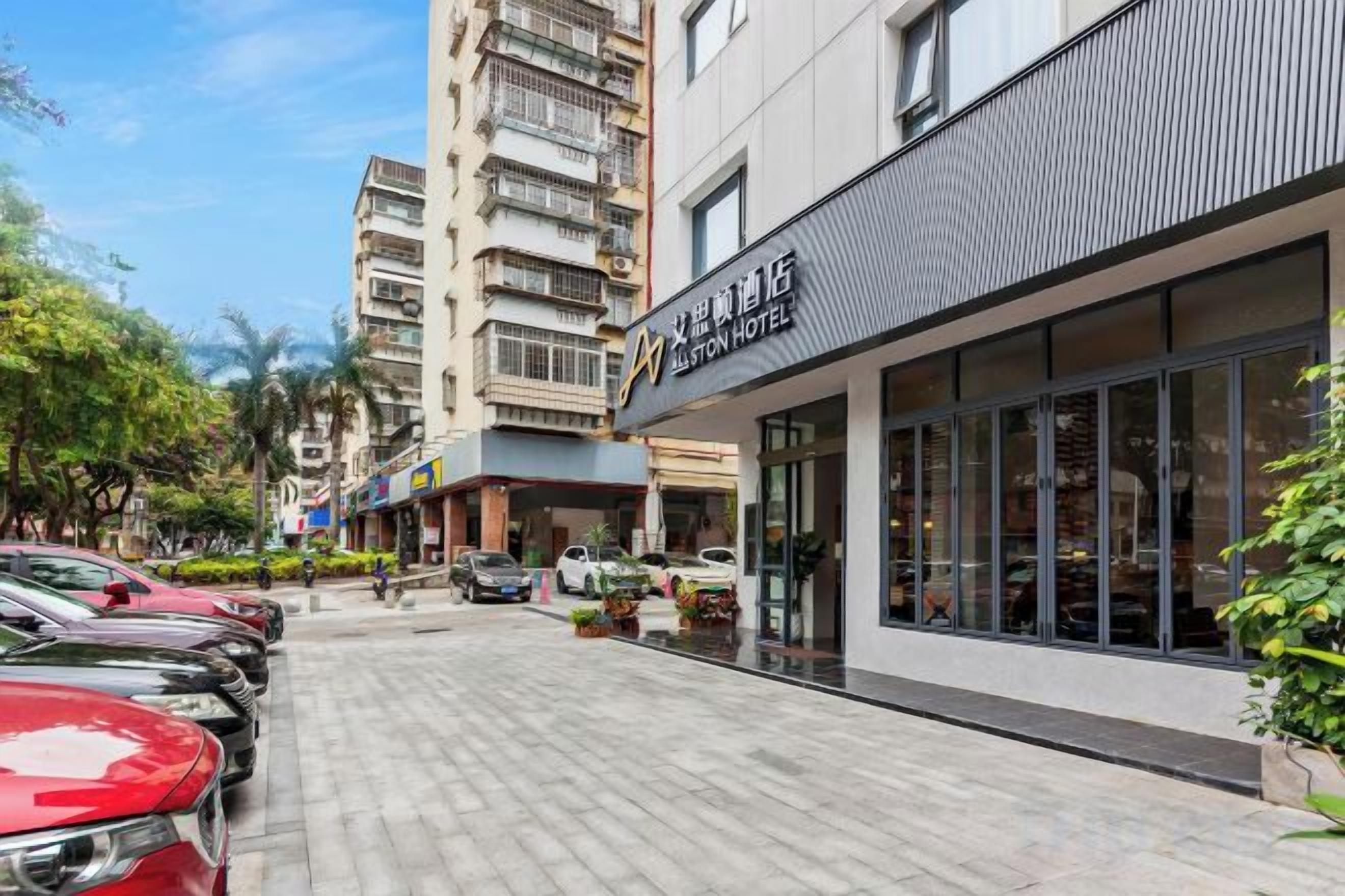A hotel with a modern facade, a parking lot, and a street with parked cars.