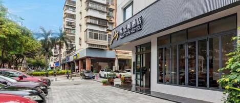 A hotel with a modern facade, a parking lot, and a street with parked cars.