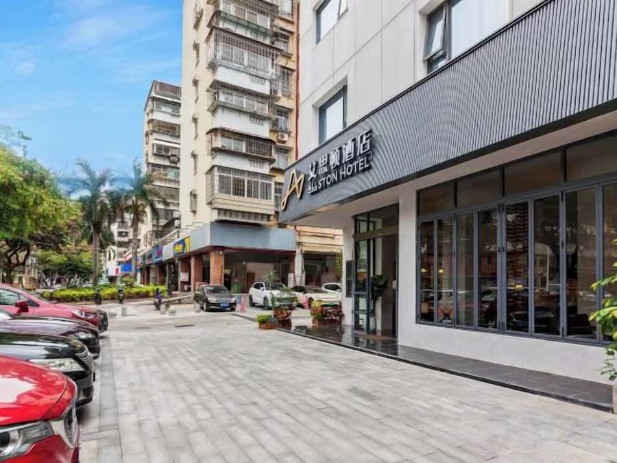 Um hotel com fachada moderna, estacionamento e uma rua com carros estacionados.