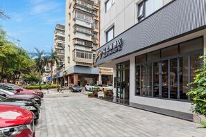 A hotel with a modern facade, a parking lot, and a street with parked cars. - Xiamen Aston Hotel (Zhongshan Road · Bailuzhou Park Branch)​ (Xiamen)