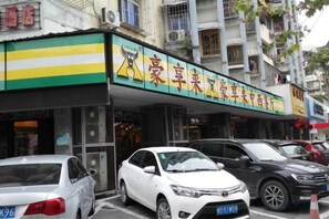 A storefront with a green and yellow awning, a sign with Chinese characters, and several parked cars in front. - Xiamen Aston Hotel (Zhongshan Road · Bailuzhou Park Branch)​ (Xiamen)