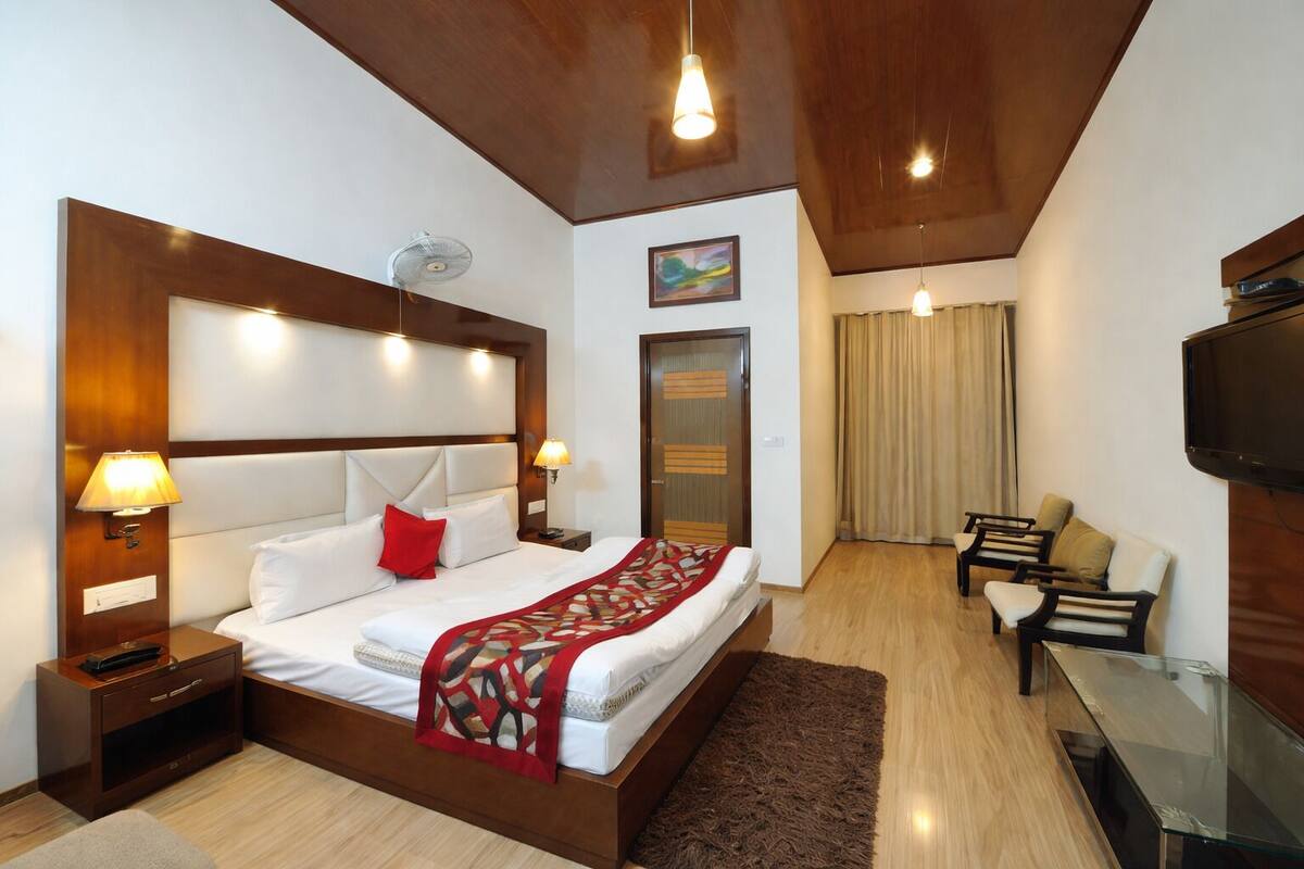 A hotel room with a bed, bedside lamps, a TV, a desk, and a chair.