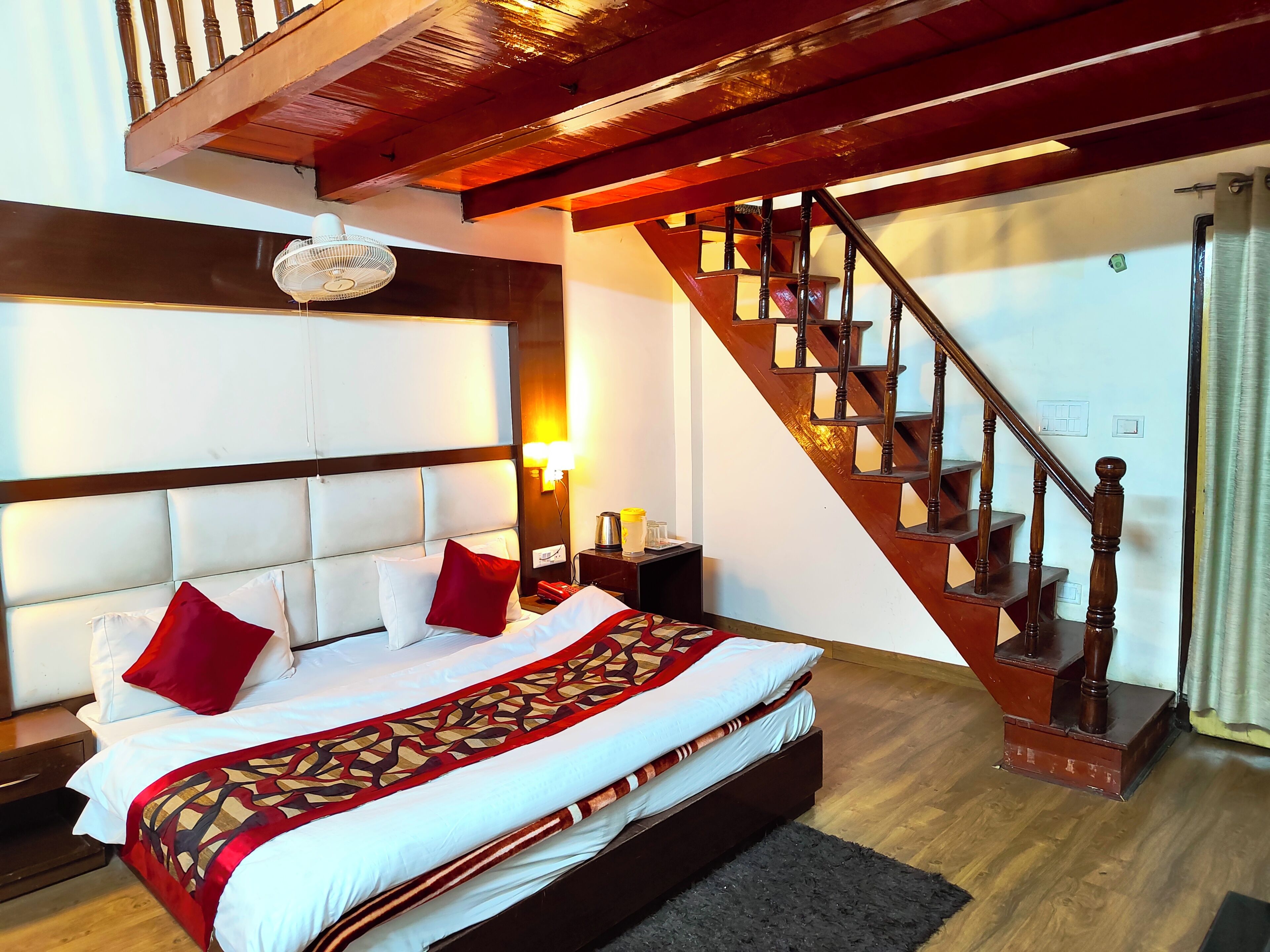 A hotel room with a large bed, a wooden staircase, and a headboard with a light fixture.