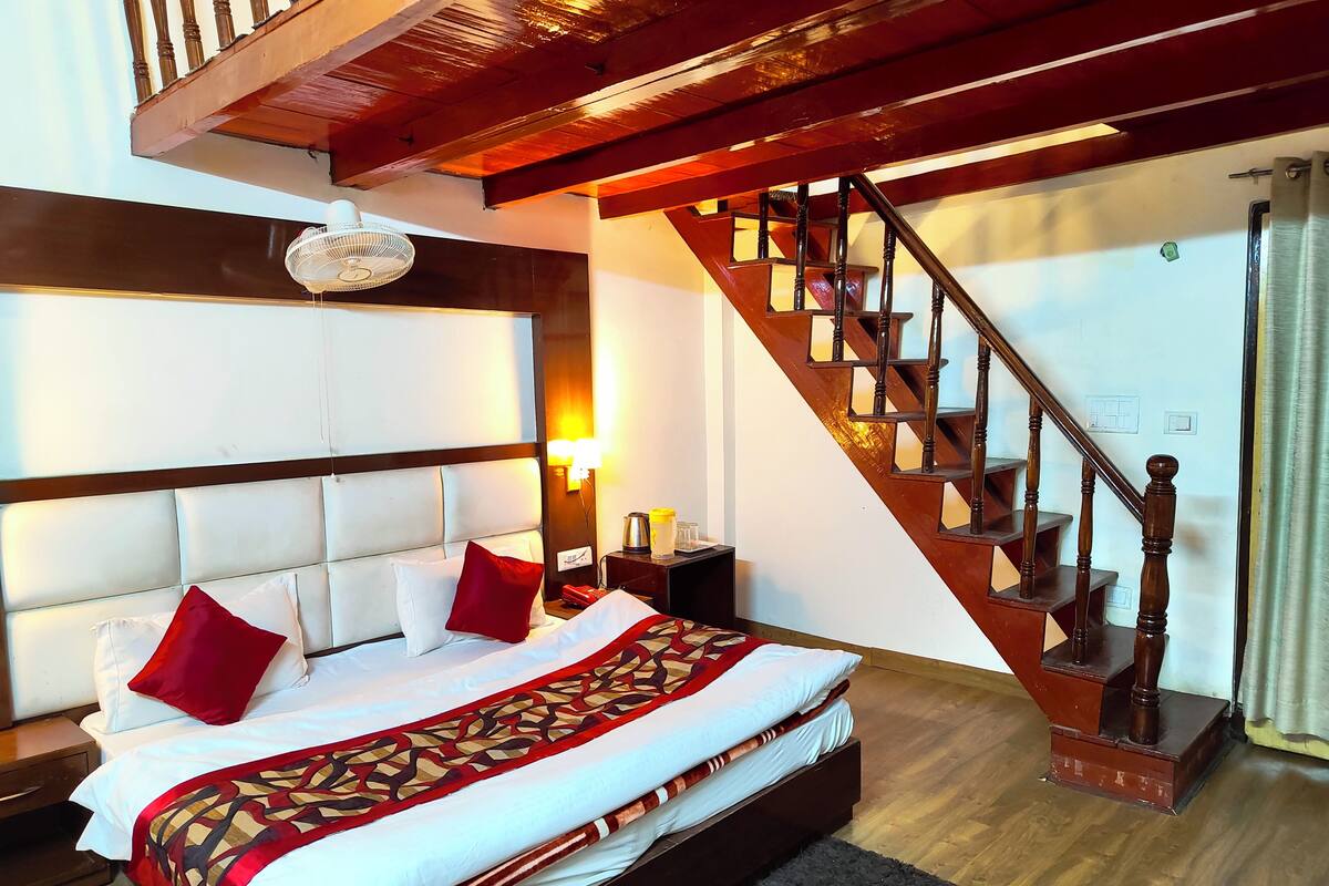A hotel room with a large bed, a wooden staircase, and a headboard with a light fixture.