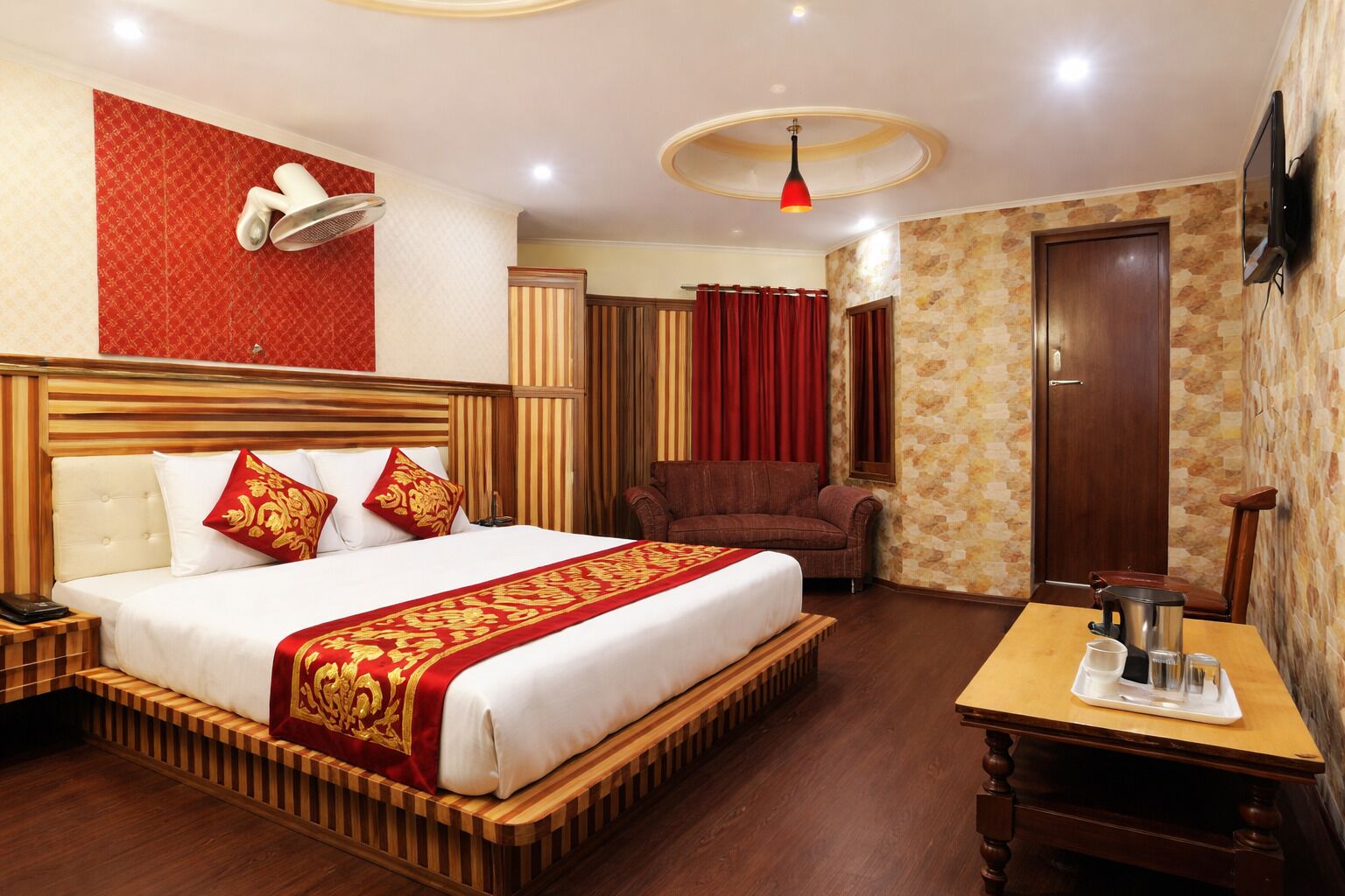 A hotel room with a large bed, a wooden headboard, a bedside table, a TV, and a red curtain.
