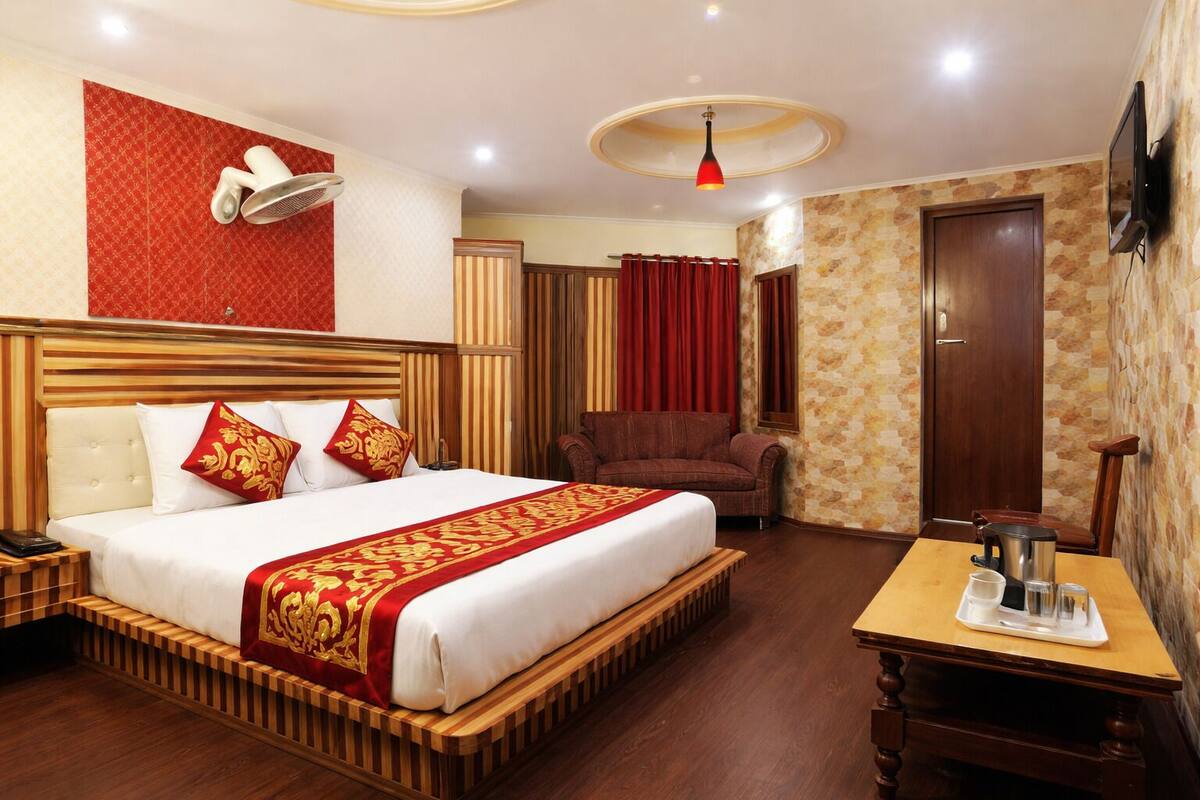 A hotel room with a large bed, a wooden headboard, a bedside table, a TV, and a red curtain.