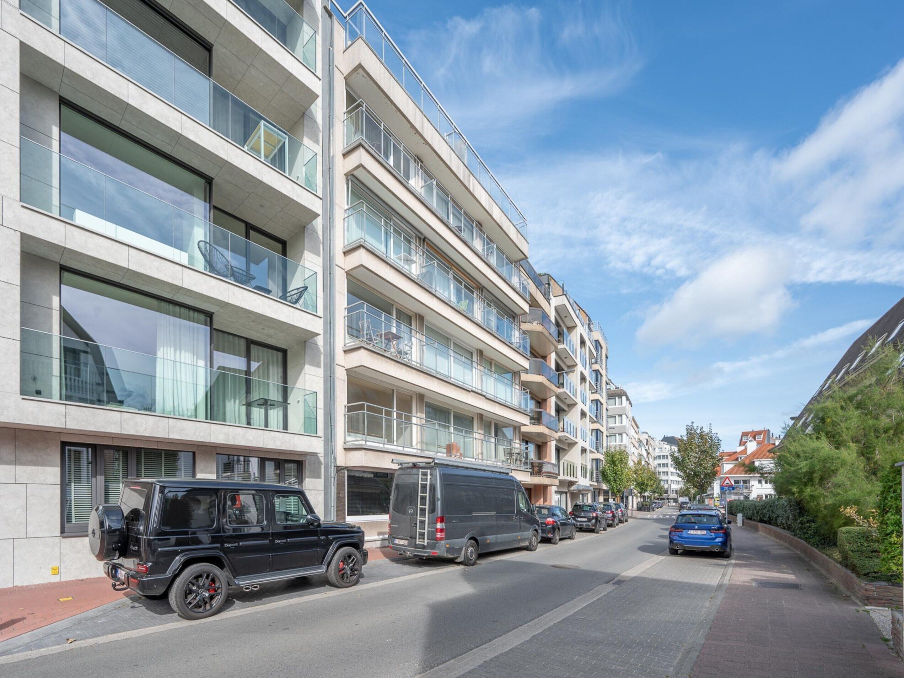 Um edifício residencial com várias andares, varandas, veículos estacionados e céu claro.