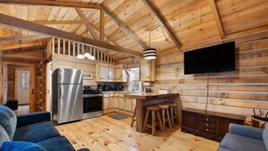 A wooden cabin interior with a kitchen, dining area, and seating.