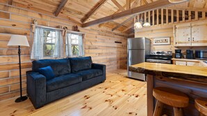 A cozy cabin interior with a wooden interior, a sofa, a dining table, and a kitchen area with appliances.