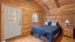A log cabin bedroom with a bed, a nightstand, a door, and a window.