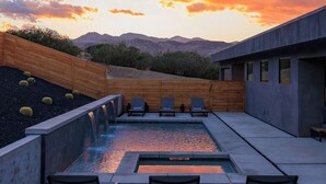 Une piscine extérieure agrémentée d’une cascade, entourée de chaises longues et d’une terrasse en bois.