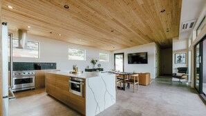 Une cuisine moderne dotée d’un grand îlot central, d’un plafond en bois et d’appareils électroménagers intégrés.