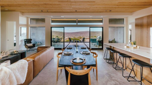 Un espace repas moderne avec une longue table, des chaises en bois et des tabourets de bar.