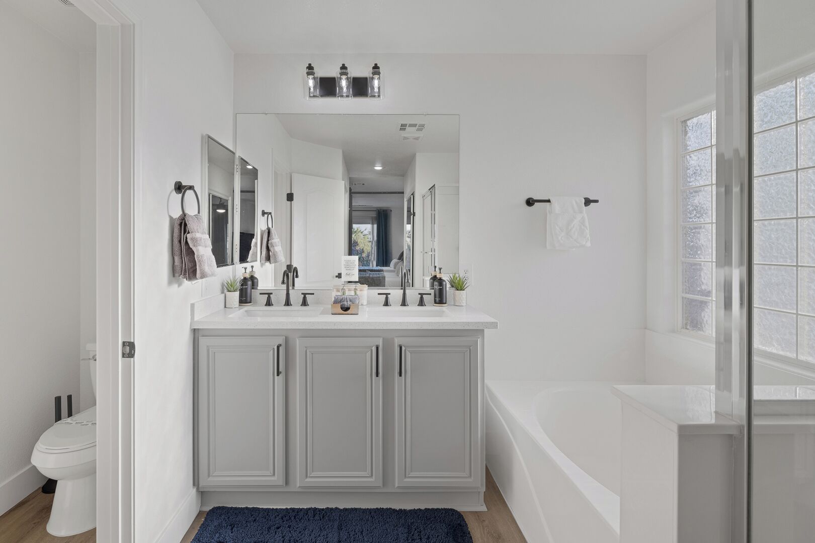 A modern bathroom with a double sink vanity, a large mirror, and a bathtub.