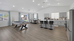 Un grand espace de vie comprenant une table de billard, des tabourets de bar, une table à manger et une cuisine équipée d’appareils électroménagers modernes.