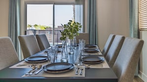 Une table à manger dressée pour six personnes, avec des chaises, un vase rempli de verdure et des verres transparents.