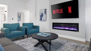 Un salon moderne doté d’un grand téléviseur à écran plat fixé au mur, d’une cheminée et de deux fauteuils de couleur turquoise.