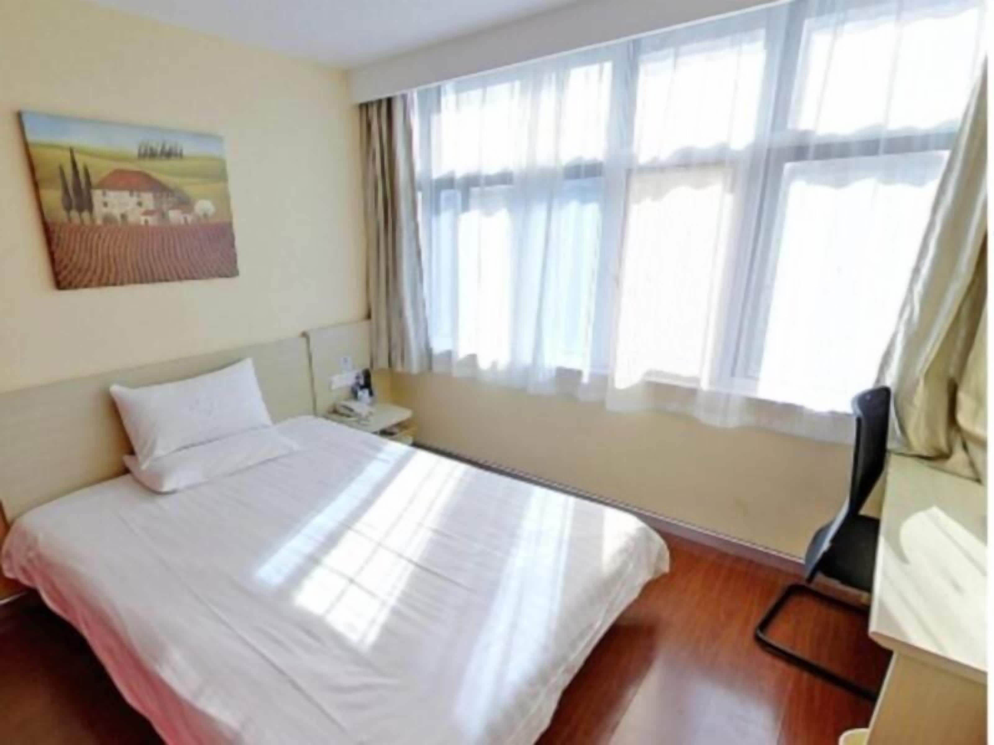 Una habitación de hotel con cama, mesita de noche, escritorio y ventana con cortinas.