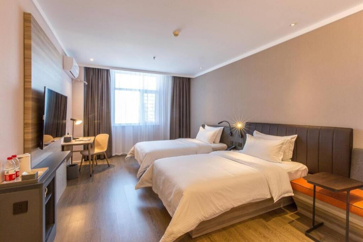 A hotel room with two beds, a desk, a TV, and a window with curtains.