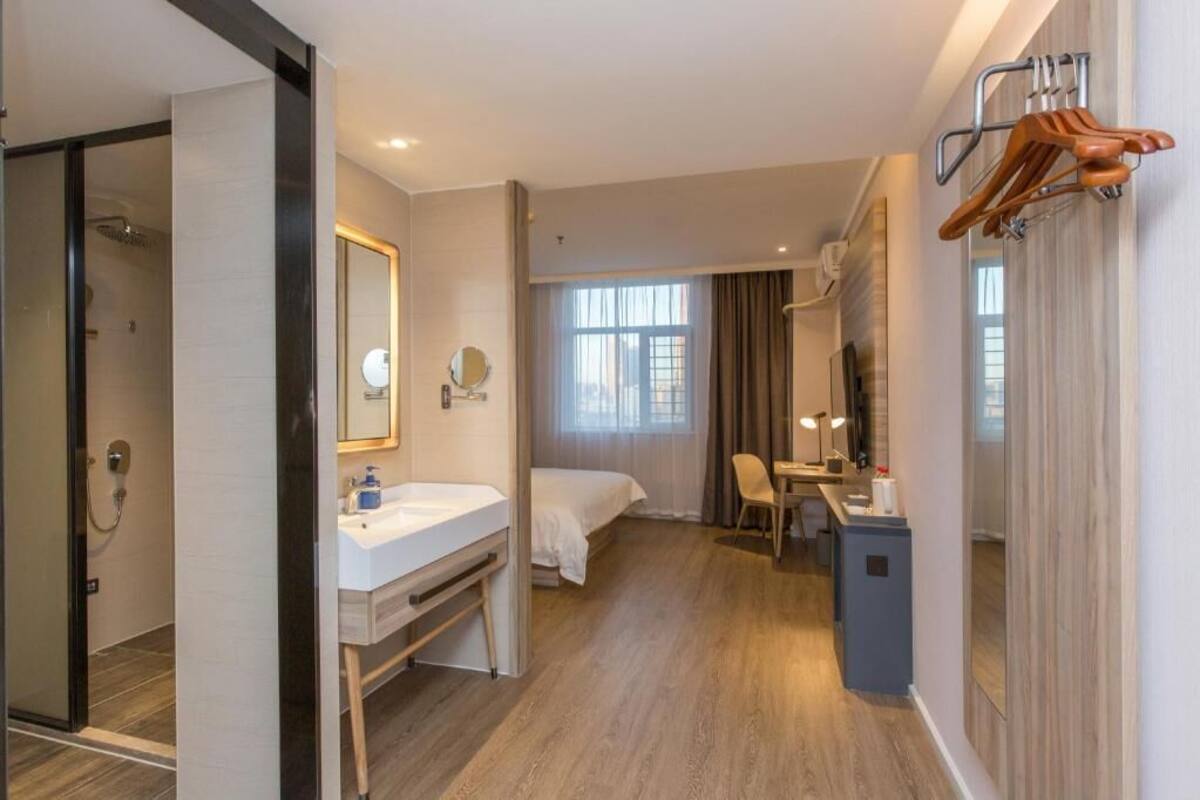 A hotel room with a shower, a bed, a desk, a chair, a mirror, and a window.