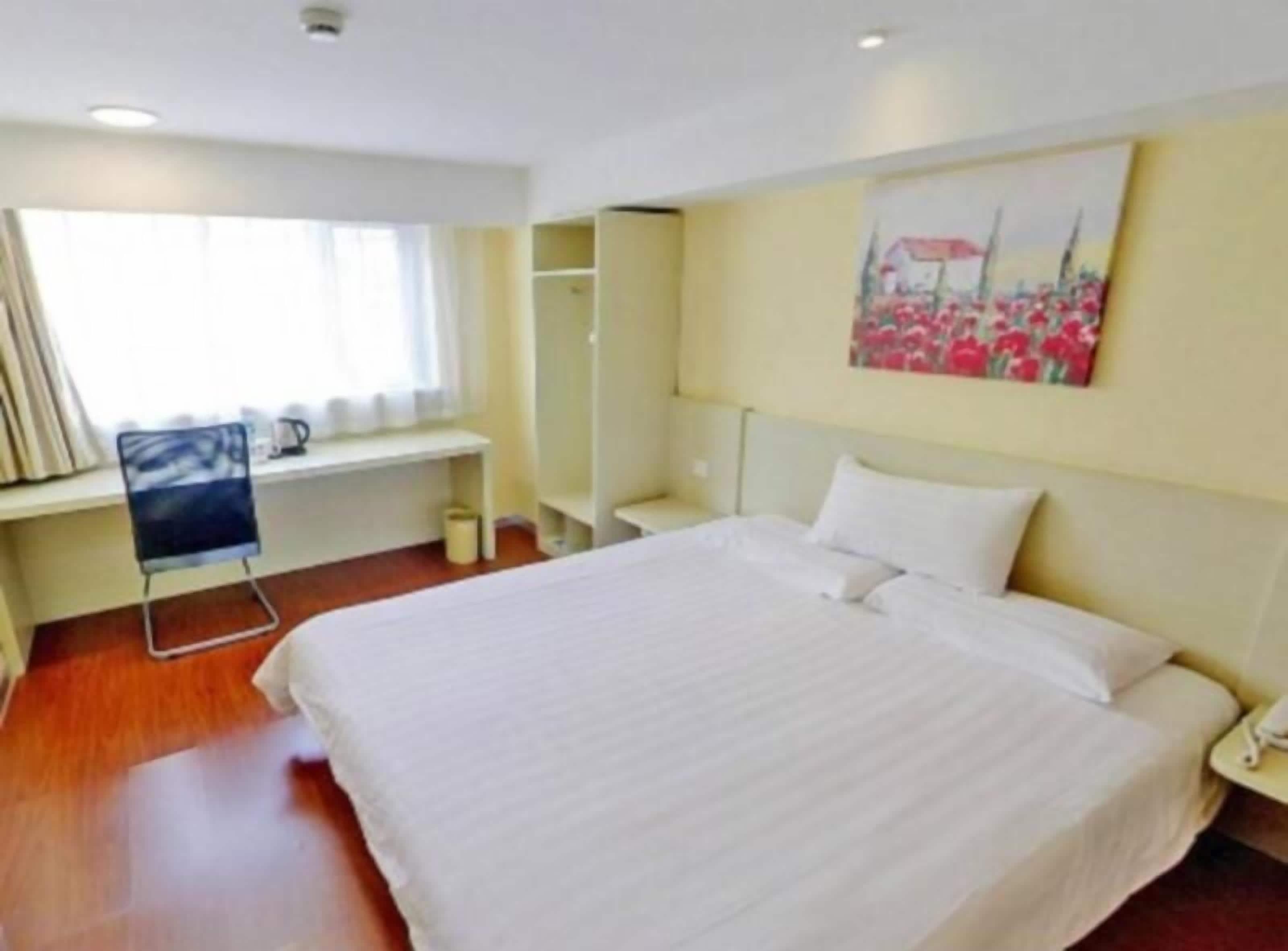 Una camera d'albergo con un letto grande, una scrivania con una sedia, una finestra con tende e un quadro appeso al muro.