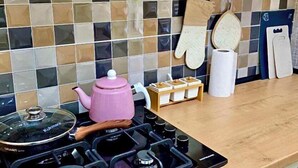 Una cucina moderna con piano cottura a gas, bollitore rosa e parete piastrellata.