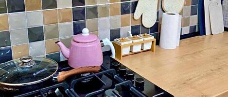 A modern kitchen with a gas stove, a pink kettle, and a tiled backsplash.