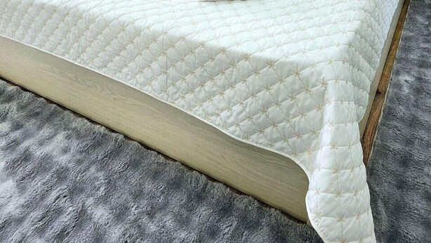 Un letto rifatto con un piumone bianco trapuntato, due cuscini e asciugamani piegati su una testiera in legno.