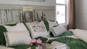 A bed with green and white bedding, a tray with flowers, and a sign on the wall. - Tiny lakefront cabin at Loon Straits on Lake Winnipeg. Perfect for couples! (Loon Straits)