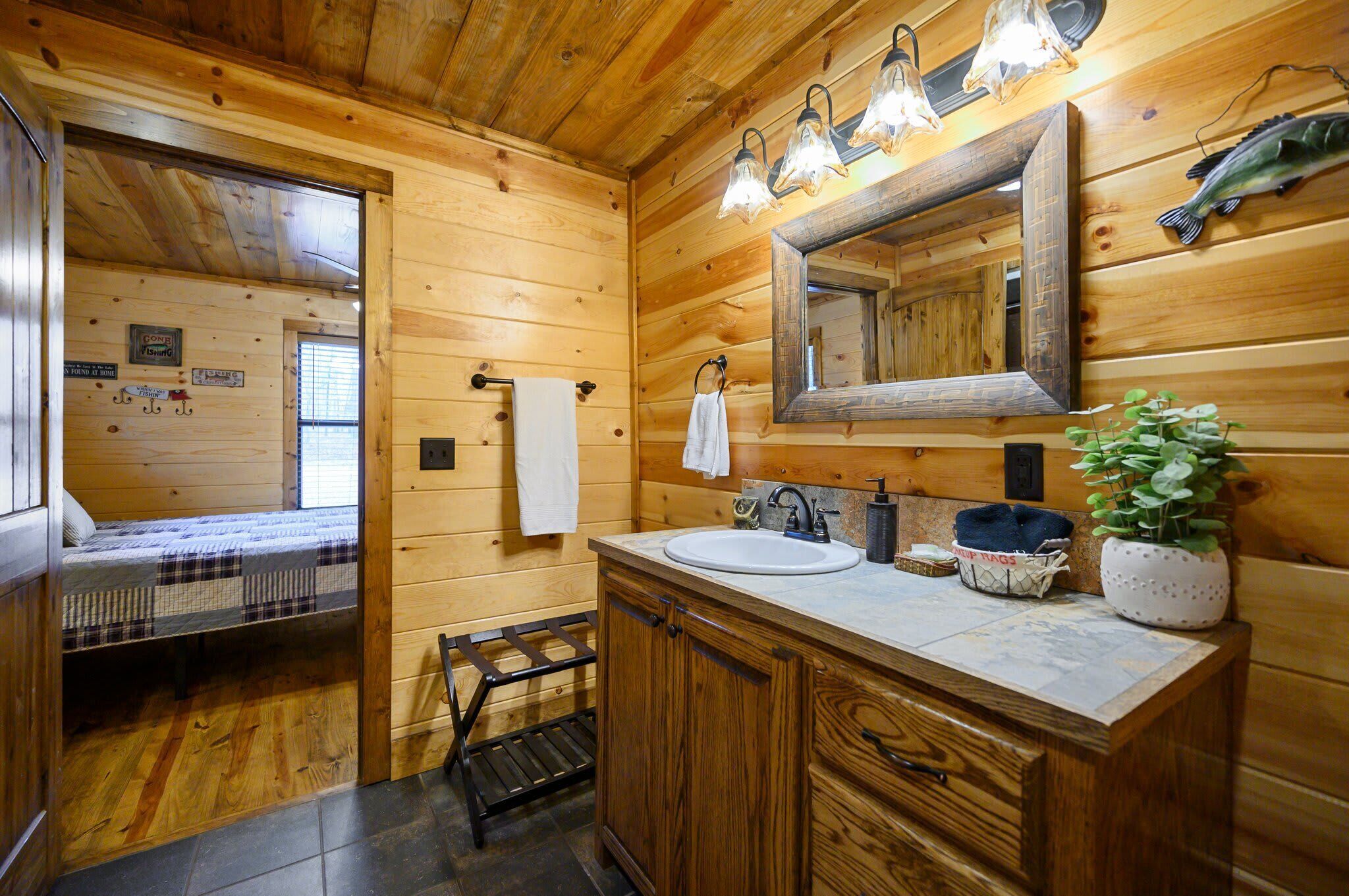A wooden cabin-style bathroom with a sink, mirror, towel rack, and a small plant.