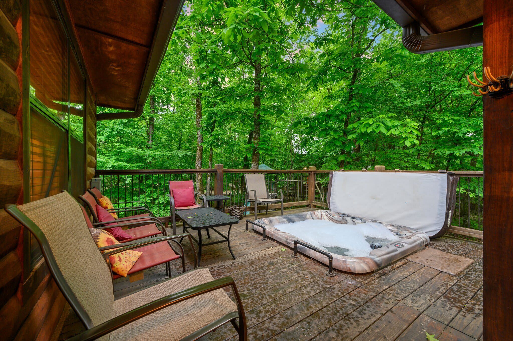 A wooden deck with outdoor seating, a hot tub, and a view of lush green trees.