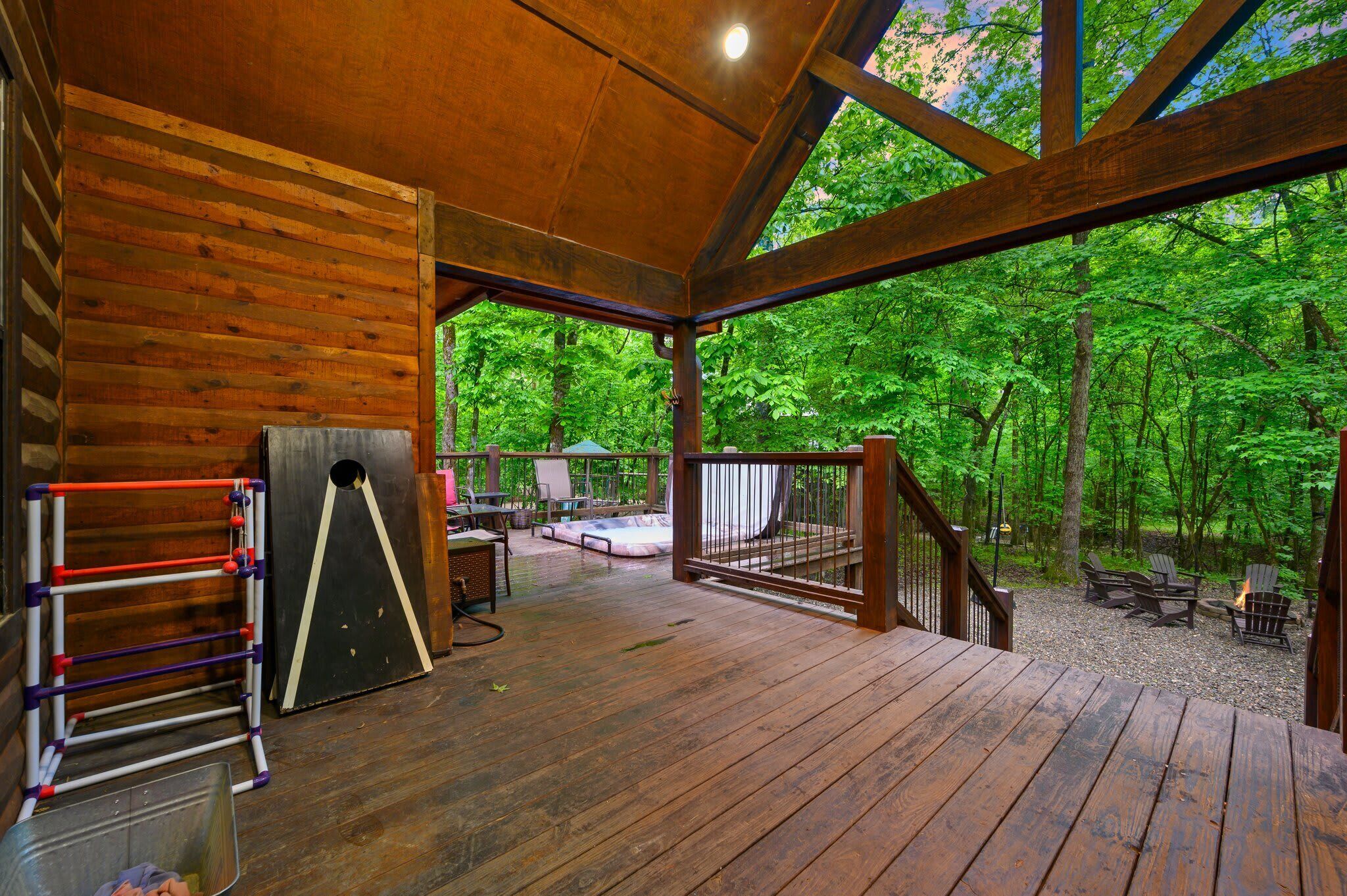A wooden deck with a view of a forest, a trampoline, and a fire pit area.