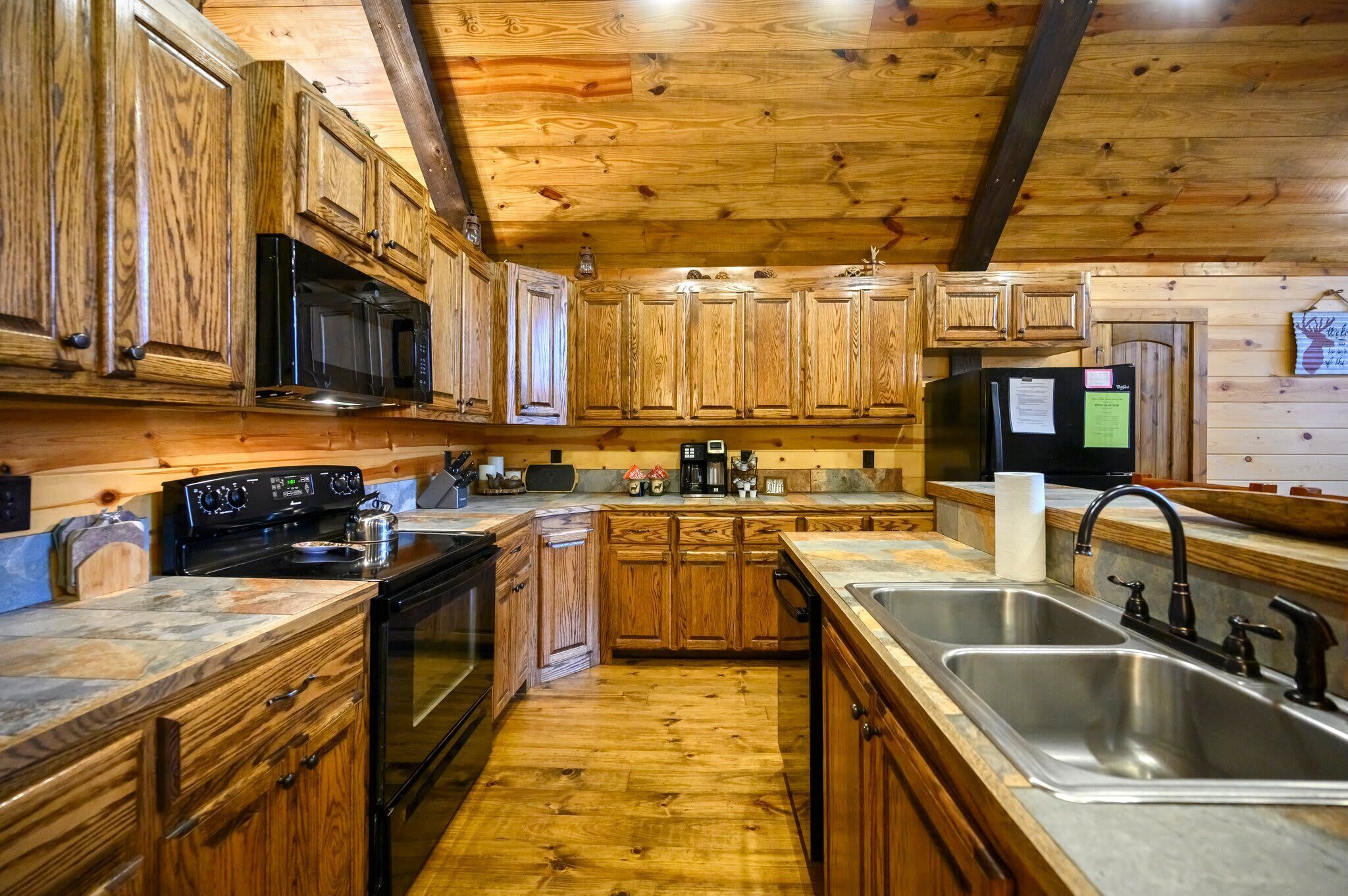 Una cocina con armarios de madera, microondas, estufa, pileta y refrigerador.