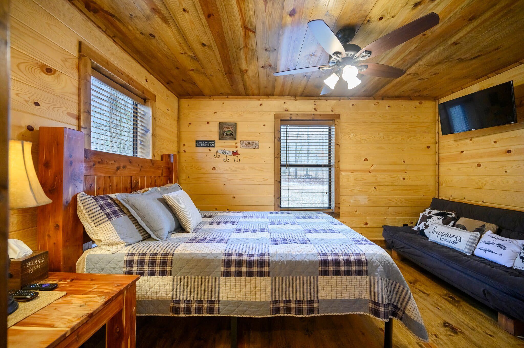 Una habitación acogedora tipo cabaña de madera con cama, sofá, ventilador de techo y televisor.