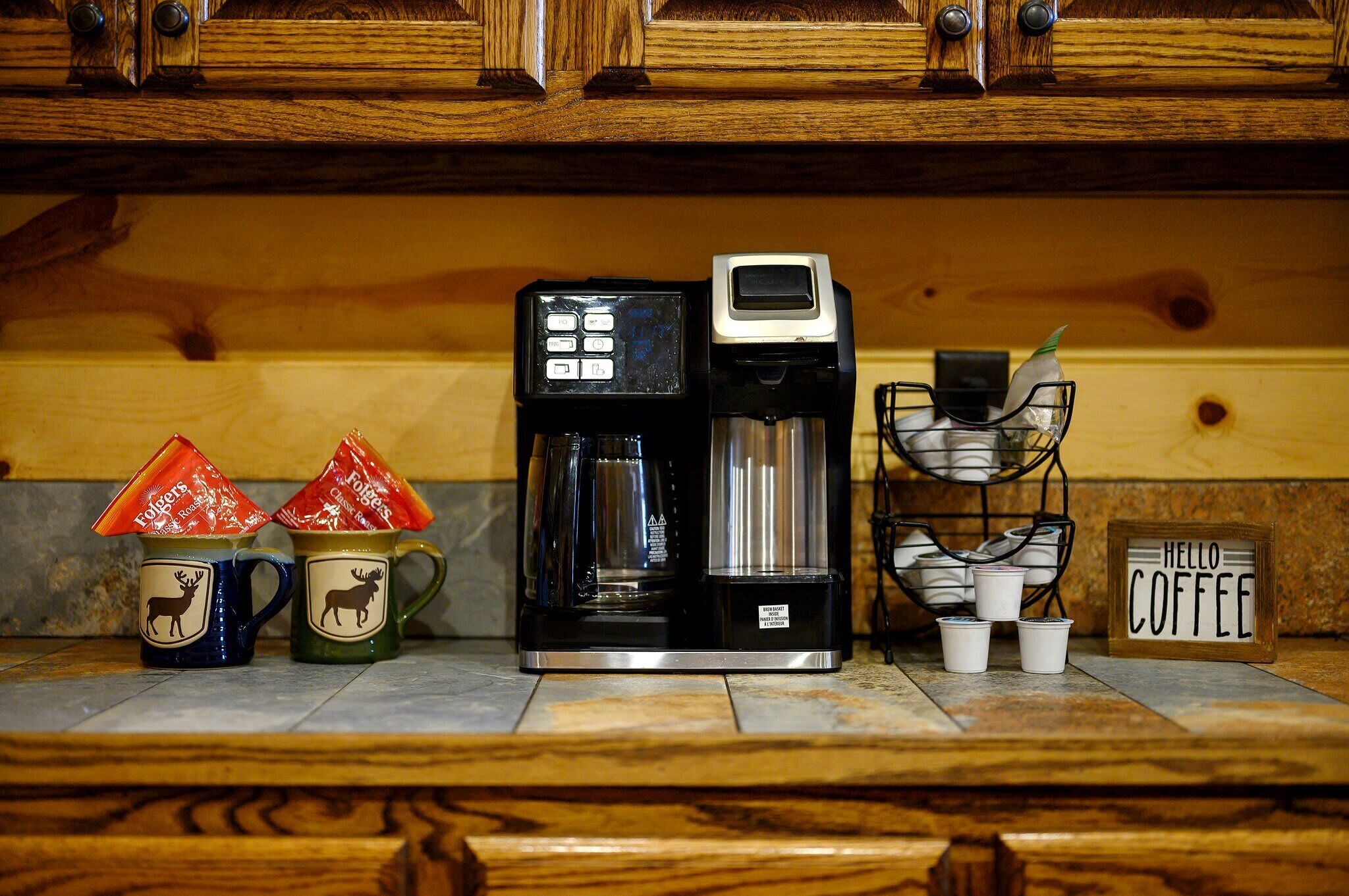 A coffee maker, two mugs with deer designs, and a 'Hello Coffee' sign on a kitchen counter.