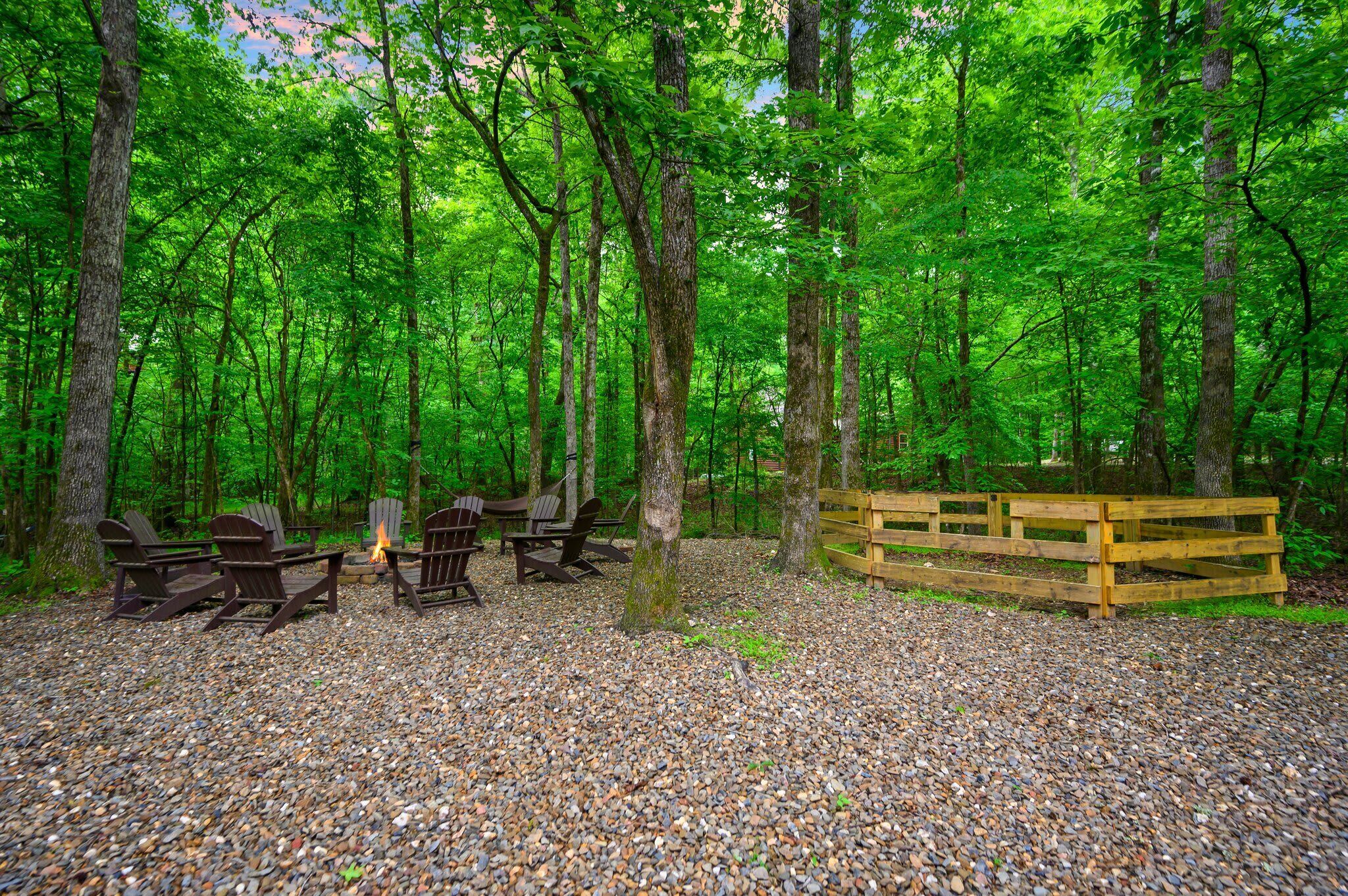 Ein bewaldeter Campingplatz mit Feuerstelle, Sitzbereich und Holzzaun.