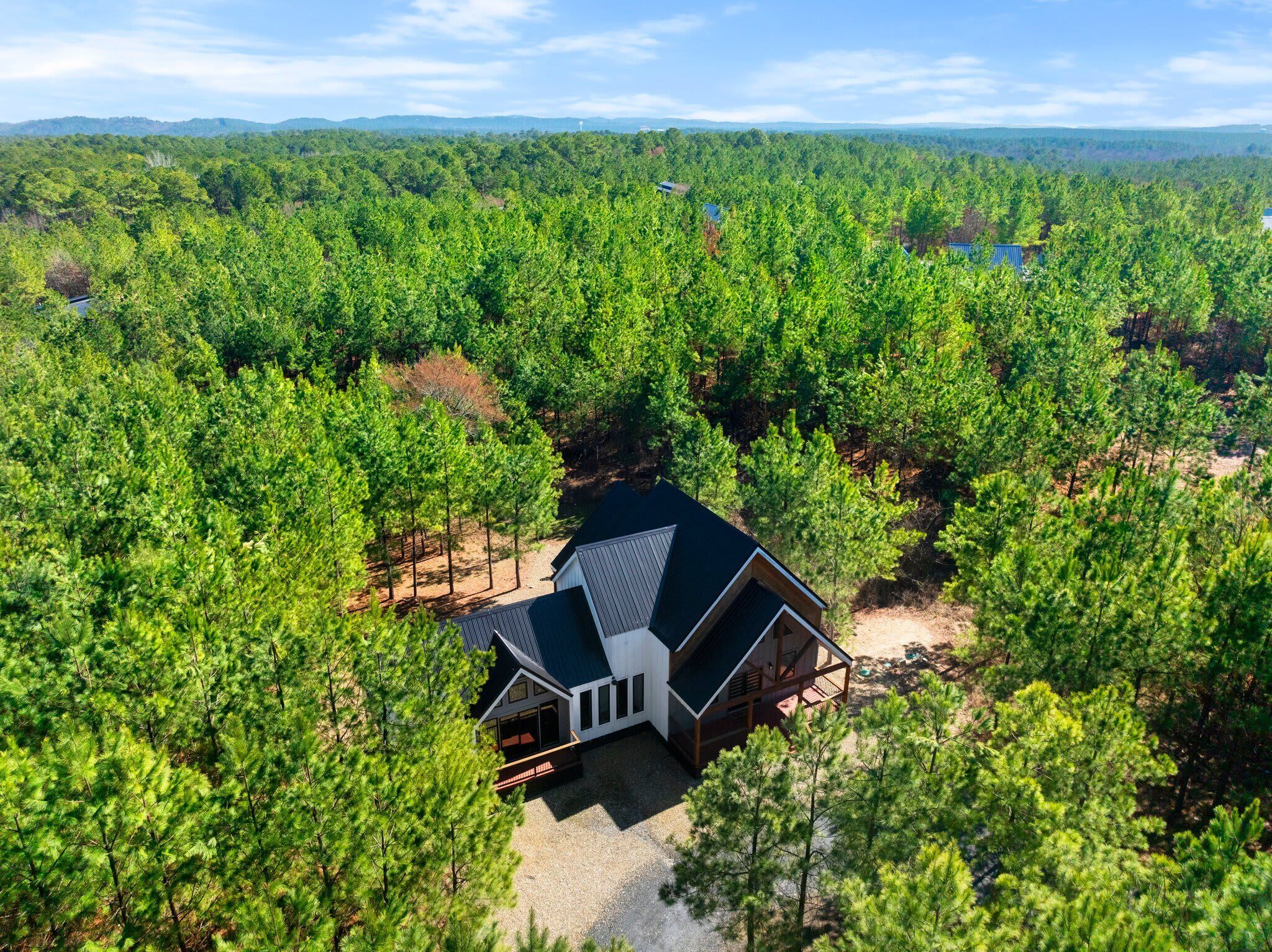 A single-story house with a dark roof, surrounded by dense forest.