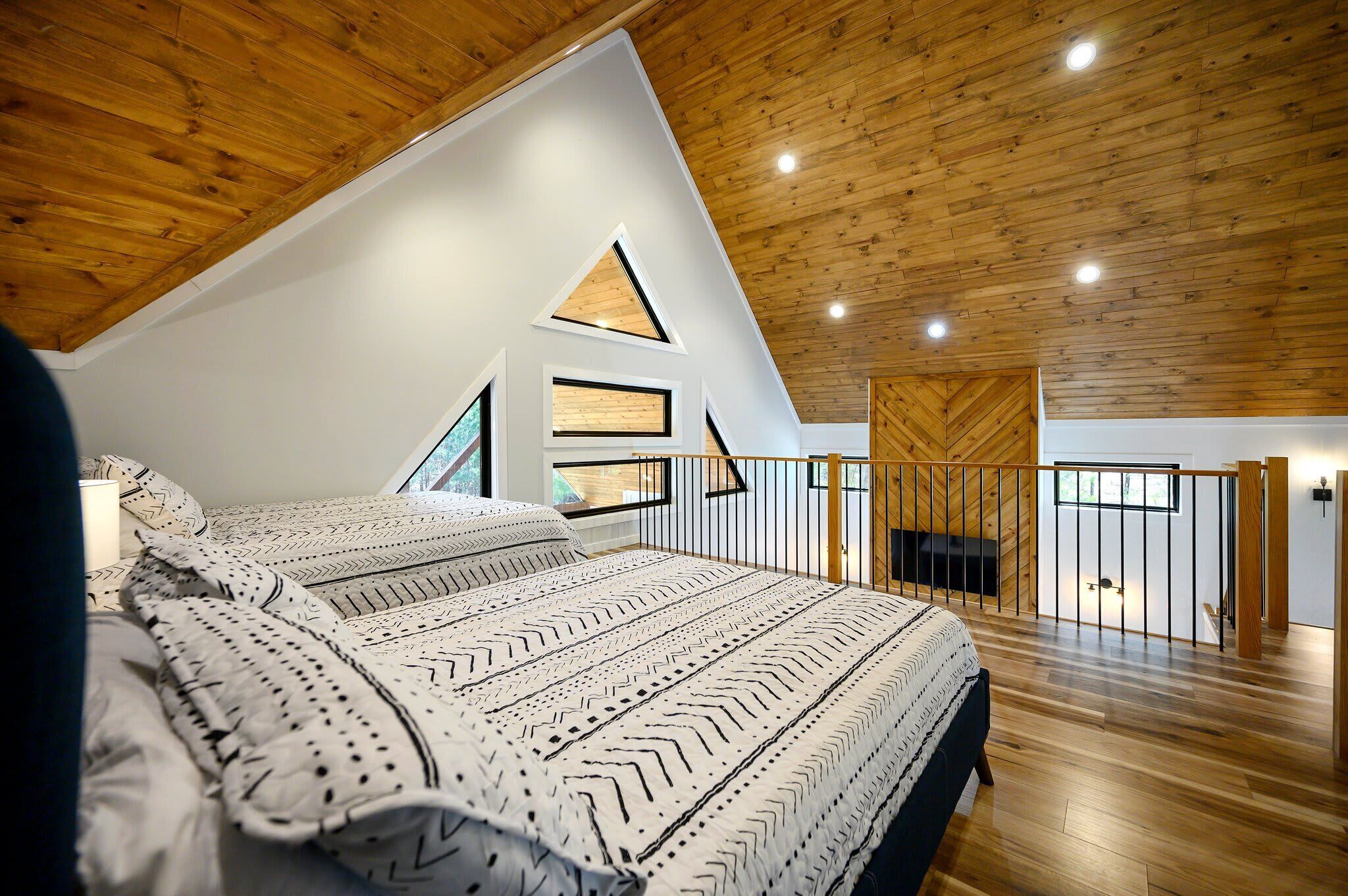 A bedroom with a sloped ceiling, wooden flooring, a bed with patterned bedding, and a view of a fireplace.